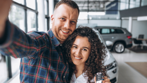 Foto de casal sorridente em uma concessionária para ilustrar artigo sobre como juntar dinheiro para comprar um carro
