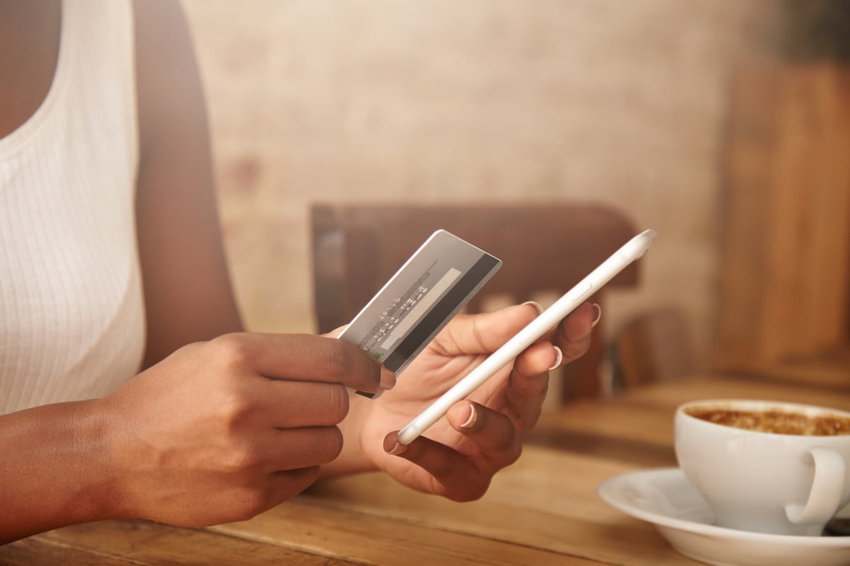 Pessoa com celular e cartão de crédito nas mãos