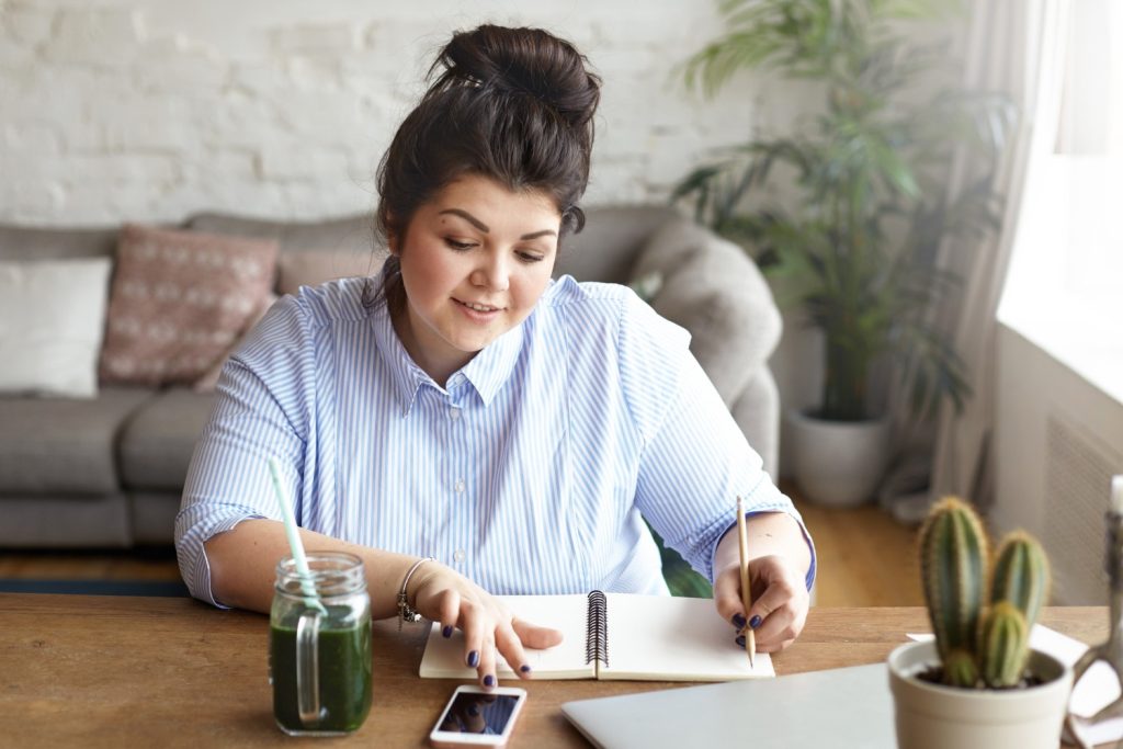 Foto de uma mulher jovem fazendo anotações em um caderno para ilustrar artigo da Cresol sobre onde investir 1000 reais